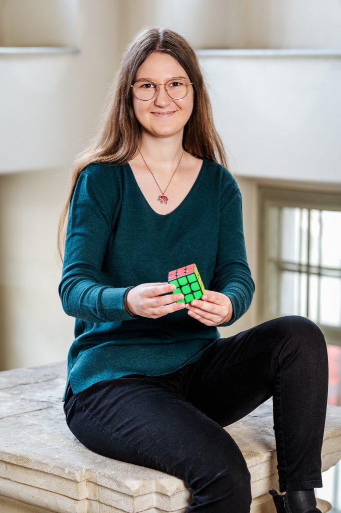 Das Portrait von Isabella Kainer zeigt sie mit einem Rubikwürfel in den Händen haltend