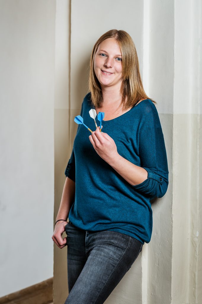 Das Portrait von Jasmin Gruber zeigt sie mit drei Dartpfeilen in der Hand