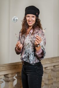 Das Portrait von Julia Pirkenau zeigt sie mit einer schwebenden Diskokugel und zwei Sternspritzern in den Händen
