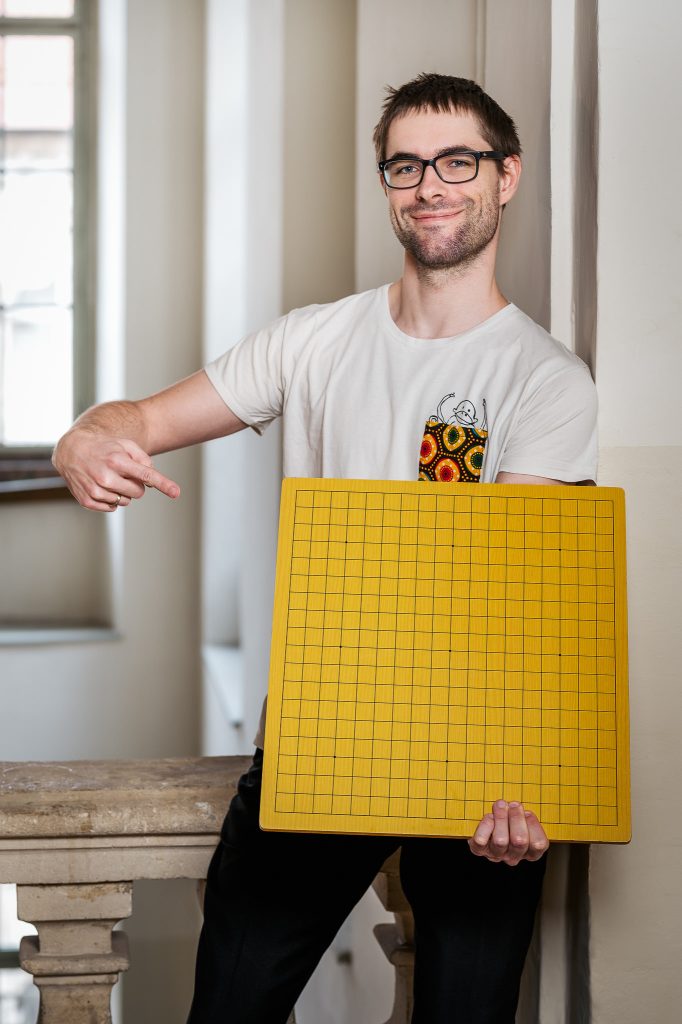 Das Portrait von Martin Unger zeigt ihn mit einem Go-Spielbrett, auf das er mit seiner rechten Hand deutet