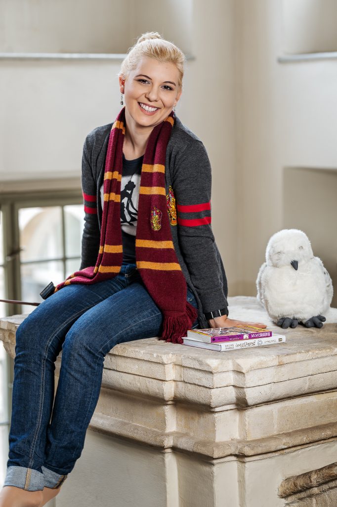 Das Portrait von Rebekka Aigner-Carmichael zeigt sie mit Büchern, einem Harry Potter Schal und zugehöriger Eule