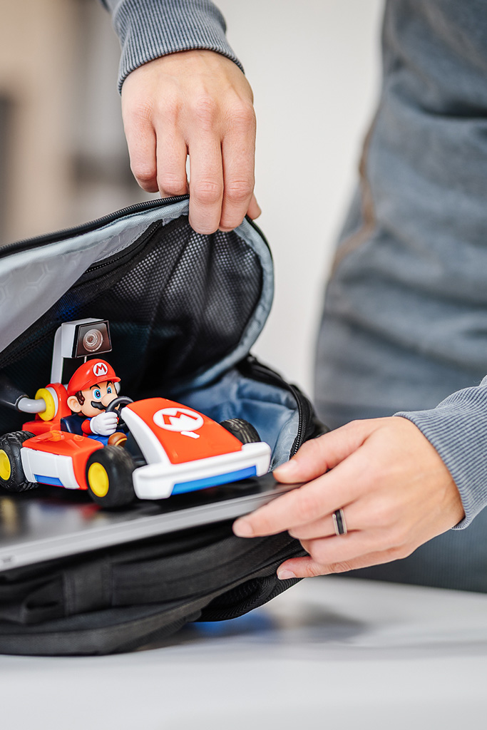 Auf dem Bild sieht man die Hände einer Person, wleche einen Rucksack mit einem Laptop und einem fernsteuerbaren MarioKart-Auto packt.