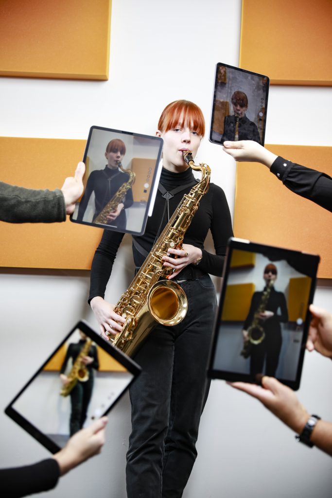 Eine Saxophonistin beim Spiel. Vor ihr halten vier Personen iPads im Fotomodus in verschiedensten Positionen.